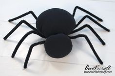 a black spider made out of foam sitting on top of a white wooden floor next to an orange ball