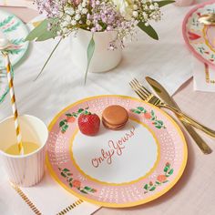 a pink and yellow plate with two strawberries on it next to a cup of tea