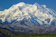 the mountains are covered with snow and green grass in front of it is a clear blue sky