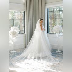 a woman in a white wedding dress standing by a window with her veil pulled back