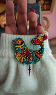 a woman's hand holding a colorful bird brooch