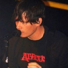 a young man holding a microphone in front of his face and wearing a black shirt with red letters on it