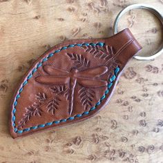 a leather keychain with a dragonfly on it's back and blue stitching