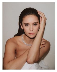 a woman in a white dress with her hand on her head and wearing a necklace