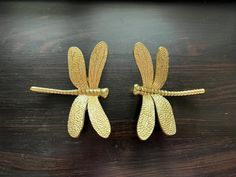 two gold dragonflys sitting on top of a wooden table next to each other