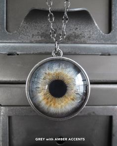 an eyeball pendant hangs from a chain on a metal surface with the words grey with amber accents