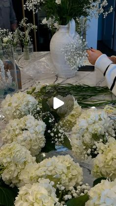 white flowers in vases sitting on a table with people looking at them from behind