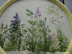 a close up of a cross stitch pattern with various flowers on it and grass in the middle