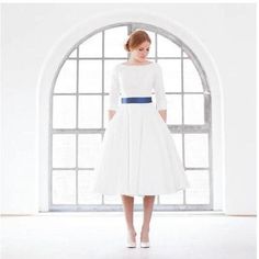 a woman in a white dress is standing by an arched window with her hands on her hips