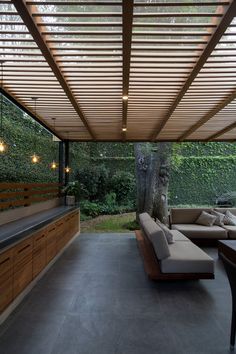 an outdoor living area with couches and tables under a pergolated roof, surrounded by greenery