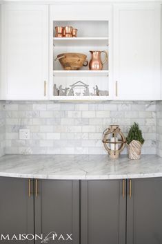 a kitchen with white cabinets and marble counter tops, along with copper accessories on the shelves