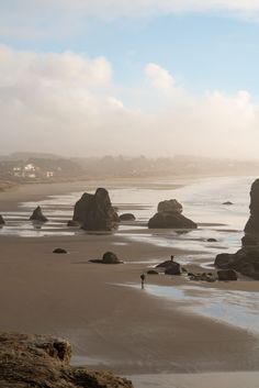 a person is standing on the beach near some rocks and water in the distance,