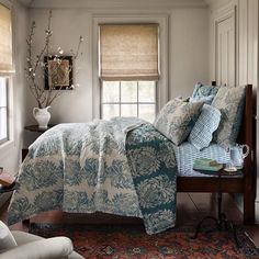 a bed sitting in a bedroom next to a window with roman shades on the windowsill