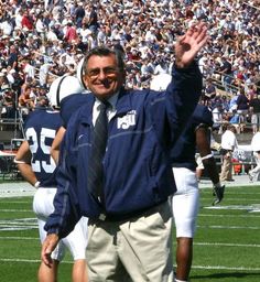 a man in a blue jacket and tie standing on a football field with his arms up