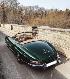 a green sports car is parked on the side of the road next to a stone wall