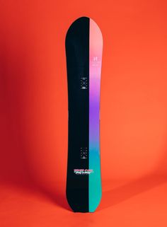 a snowboard is standing upright on an orange background with the bottom half painted pink and blue