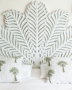 a white headboard with palm trees on it and two pillows in the foreground