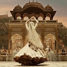 a woman is dancing in front of an ornate building with fountains and people around her