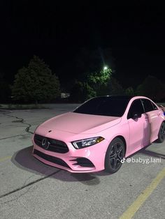 a pink mercedes cla parked in a parking lot at night with its lights on