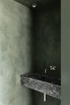 a bathroom with green walls and marble counter top in the corner, under a faucet