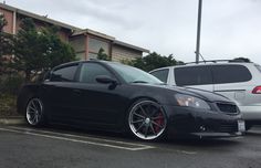 a black car parked in a parking lot next to two white cars with red rims