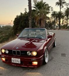 a red car parked on the side of a road next to palm tree's