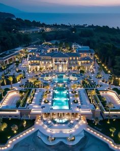 an aerial view of a mansion at night with lights on the pool and surrounding landscaping