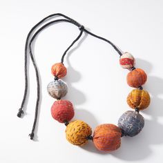 an orange and grey beaded necklace on a black cord with two balls hanging from it