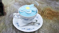 a teacup with a flower on it sitting on top of a saucer next to a pair of scissors