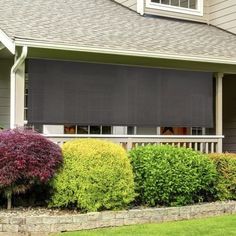 a house with some bushes in front of it and a black roller shade on the window