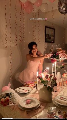 a woman in a pink dress is sitting at a table with candles and plates on it