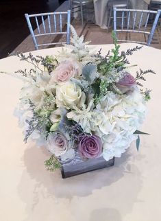 a vase filled with white and purple flowers on top of a round table covered in chairs