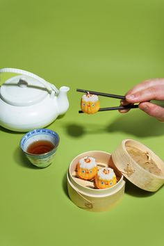 a person holding chopsticks over some food in a wooden container on a green surface