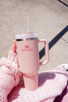 a pink starbucks cup sitting on top of a blanket next to a persons hand and sweater