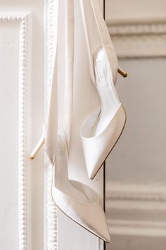 a pair of white high heels hanging from a hook on a door with a curtain in the background