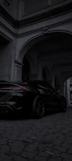 a black sports car parked in front of an arched doorway with light coming from it