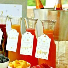 three different types of drinks on a table with tags attached to the bottles and bowls full of fruit