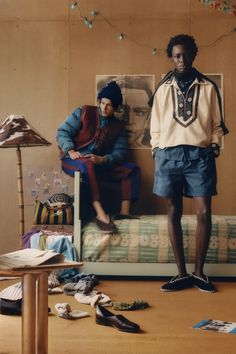 two people standing in front of a bed with shoes on the floor next to it