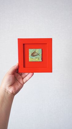 a hand holding up a small red box with a painting on the inside of it