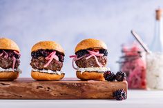 three hamburgers with meat, cheese and blackberries are sitting on a cutting board