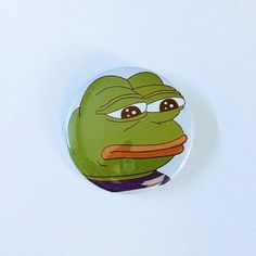 a button with a frog face on it's side and eyes wide open, sitting on a white surface