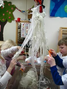 three children are playing with yarn and scissors