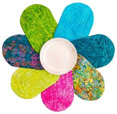 a colorful flower made out of different colored pieces of cloth and fabric with a white bowl in the center