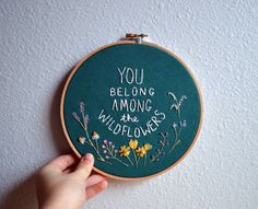 a hand embroidered hoop with the words you belong among the wildflowers on it