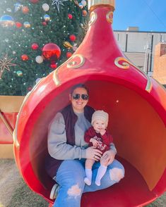 a woman and child are sitting in a large red object with a christmas tree behind them