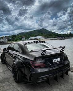 a black car parked on the side of a body of water with dark clouds in the background