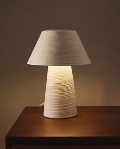 a white lamp sitting on top of a wooden table next to a night stand and wall