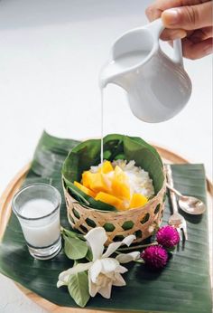 a person pouring milk into a bowl filled with fruit and vegetables on top of a banana leaf