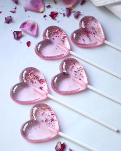 four heart shaped lollipops sitting on top of a white table next to pink flowers