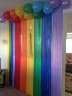 there is a rainbow colored curtain with balloons hanging from it's sides in the room